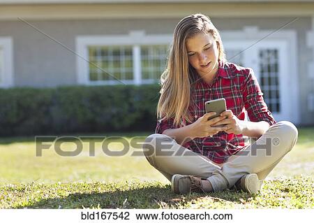 Stock Image - Caucasian girl using cell phone in backyard. Fotosearch
