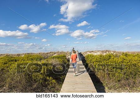 Stock Image - Caucasian girl walking on wooden walkway in remote field. Fotosearch