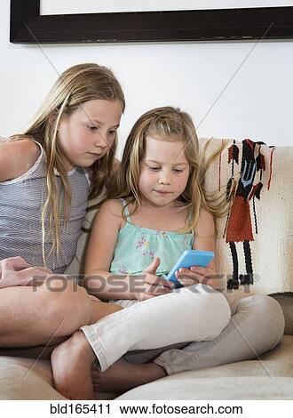 Caucasian girls using cell phone on sofa View Large Photo Image Stock Image - Caucasian girls using cell phone on sofa. Fotosearch