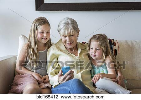 Stock Image - Caucasian grandmother and granddaughters using cell phone on sofa. Fotosearch