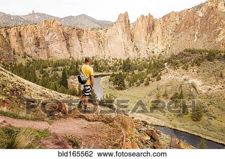 Stock Image - Caucasian hiker admiring hills and stream in desert landscape, Smith Rock State Park, Oregon, United States. Fotosearch