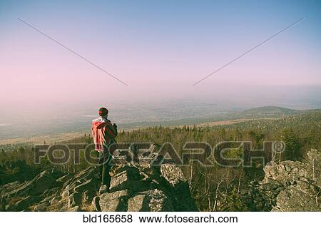 Stock Photo - Caucasian hiker admiring view from remote rock formation. Fotosearch