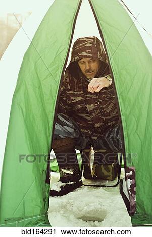 Stock Image - Caucasian hiker ice fishing in tent. Fotosearch
