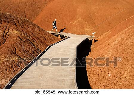 Stock Photography - Caucasian hiker on wooden walkway in desert hills. Fotosearch