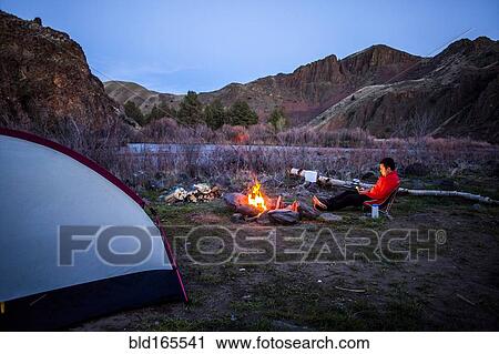 Stock Image - Caucasian hiker sitting near campfire in desert field, Painted Hills, Oregon, United States. Fotosearch
