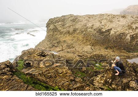 Stock Photography - Caucasian hiker sitting on cliffs over ocean, Mendocino, California, United States. Fotosearch