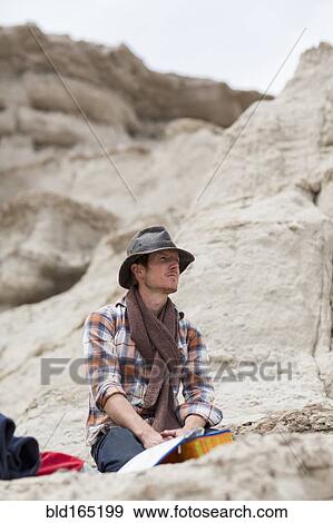 Stock Photo - Caucasian hiker sitting on rock formation in desert. Fotosearch
