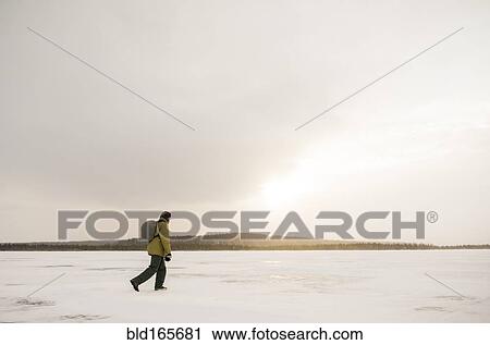 Stock Image - Caucasian hiker walking in snowy remote field. Fotosearch