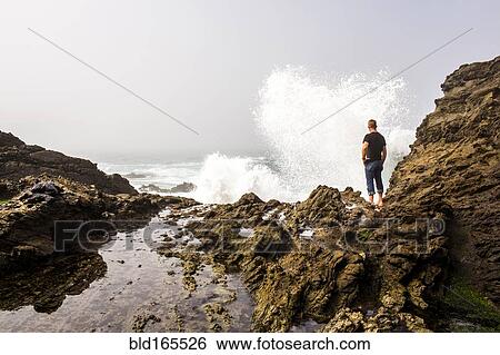 Stock Photograph - Caucasian hiker watching crashing ocean waves. Fotosearch