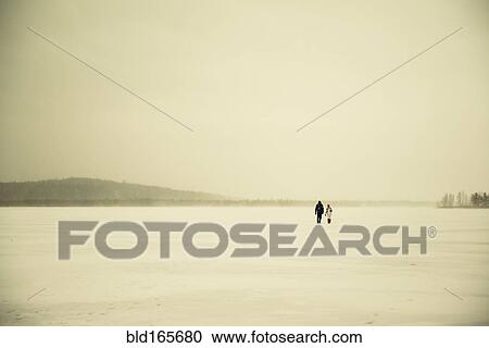 Stock Image - Caucasian hikers walking in snowy remote field. Fotosearch