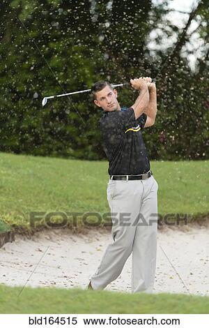 Stock Photography - Caucasian man chipping from golf course sand trap. Fotosearch