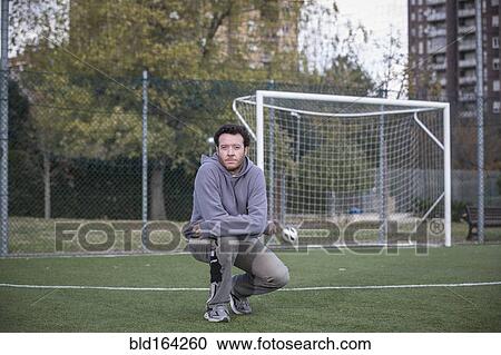 Stock Image - Caucasian man crouching on soccer field in urban park. Fotosearch