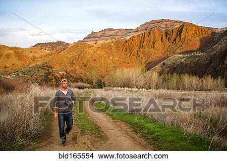 Picture - Caucasian man drinking coffee on dirt path, Painted Hills, Oregon, United States. Fotosearch