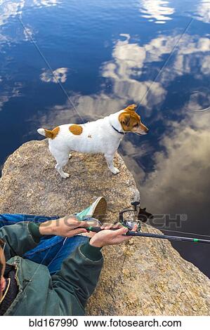 Stock Image - Caucasian man fishing with dog in remote lake. Fotosearch