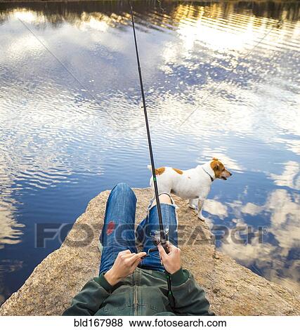 Stock Photo - Caucasian man fishing with dog in remote lake. Fotosearch