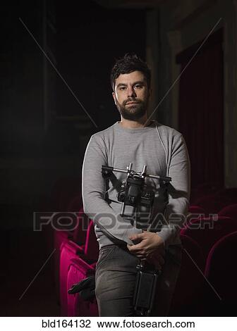 Stock Image - Caucasian man holding projector in movie theater. Fotosearch