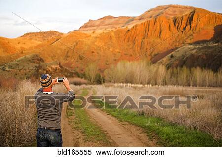 Stock Photography - Caucasian man photographing desert hills, Painted Hills, Oregon, United States. Fotosearch