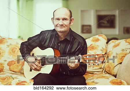 Stock Image - Caucasian man playing guitar on sofa. Fotosearch