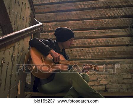 Caucasian man playing guitar on staircase View Large Photo Image Stock Photo - Caucasian man playing guitar on staircase. Fotosearch