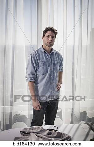 Stock Photo - Caucasian man standing near curtains in bedroom. Fotosearch