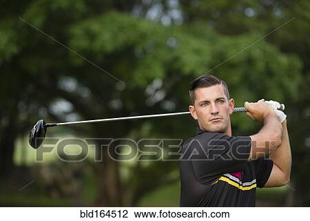 Stock Image - Caucasian man swinging club on golf course. Fotosearch