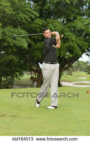 Stock Image - Caucasian man swinging club on golf course. Fotosearch