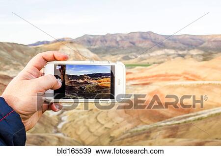 Stock Photo - Caucasian man taking cell phone photograph of desert landscape, Painted Hills, Oregon, United States. Fotosearch