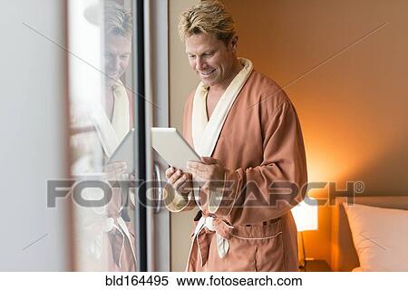 Stock Photography - Caucasian man using digital tablet at bedroom window. Fotosearch