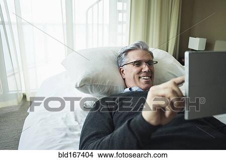Picture - Caucasian man using digital tablet in bed. Fotosearch