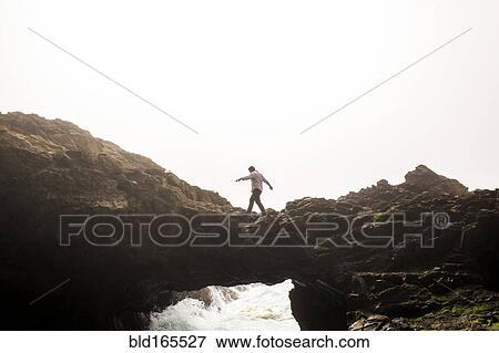 Stock Photo - Caucasian man walking on bridge over ocean waves. Fotosearch