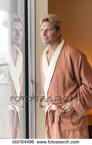 Stock Photograph - Caucasian man wearing bathrobe at bedroom window. Fotosearch