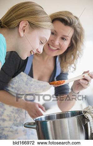 Stock Image - Caucasian mother and daughter cooking sauce in pot. Fotosearch