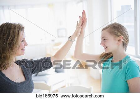 Stock Photography - Caucasian mother and daughter high fiving in living room. Fotosearch