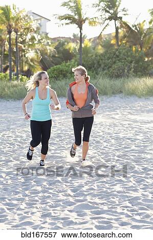 Stock Photo - Caucasian mother and daughter jogging on beach. Fotosearch