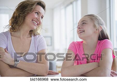 Stock Photo - Caucasian mother and daughter laughing at table. Fotosearch