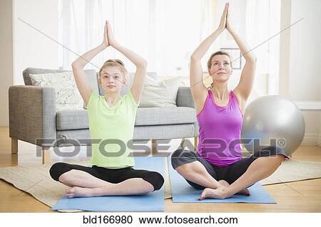 Stock Image - Caucasian mother and daughter practicing yoga in living room. Fotosearch