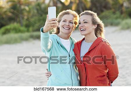 Stock Photo - Caucasian mother and daughter taking selfie on beach. Fotosearch