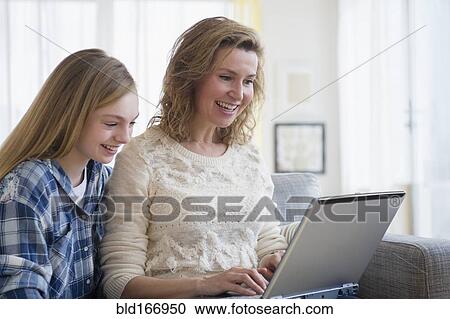 Stock Image - Caucasian mother and daughter using laptop on sofa. Fotosearch