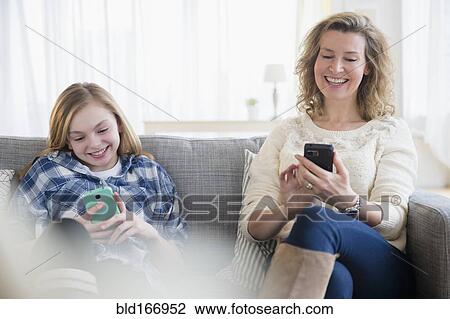 Stock Image - Caucasian mother and daughter using cell phones on sofa. Fotosearch