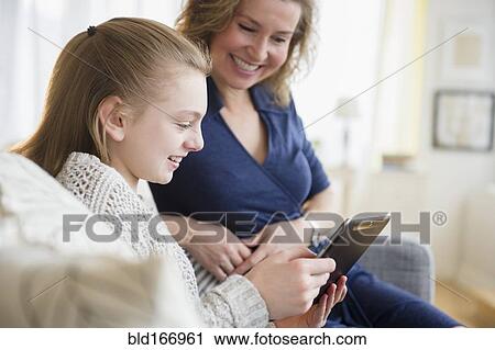 Stock Image - Caucasian mother and daughter using digital tablet on sofa. Fotosearch
