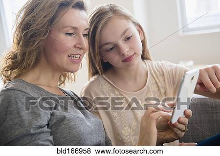 Caucasian mother and daughter using cell phone in living room View Large Photo Image Stock Photo - Caucasian mother and daughter using cell phone in living room. Fotosearch