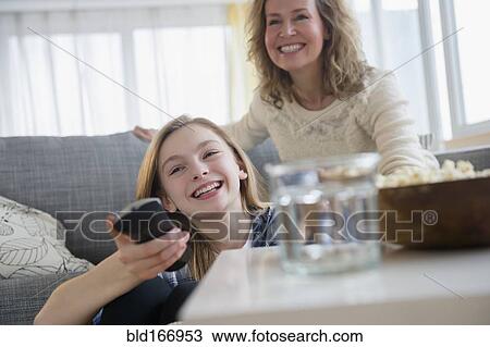 Stock Image - Caucasian mother and daughter watching television on sofa. Fotosearch