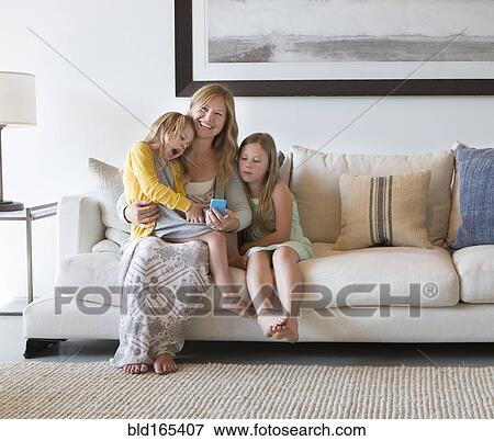 Caucasian mother and daughters using cell phone on sofa View Large Photo Image Stock Photo - Caucasian mother and daughters using cell phone on sofa. Fotosearch