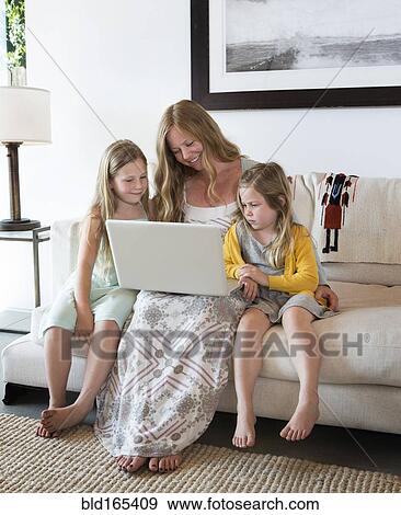 Stock Photo - Caucasian mother and daughters using laptop on sofa. Fotosearch