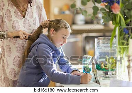 Stock Image - Caucasian mother brushing hair of daughter. Fotosearch