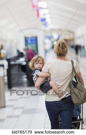 Stock Photo - Caucasian mother carrying baby son in airport. Fotosearch