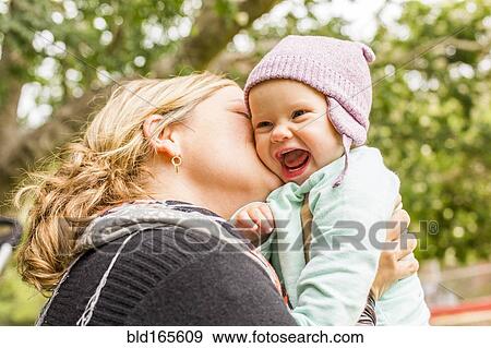 Stock Photo - Caucasian mother kissing baby daughter outdoors. Fotosearch