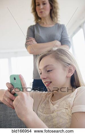 Picture - Caucasian mother watching daughter use cell phone. Fotosearch