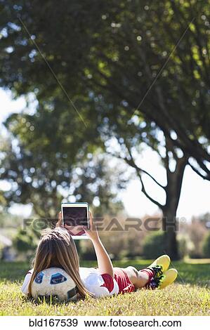 Stock Photo - Caucasian soccer player laying in grass using digital tablet. Fotosearch