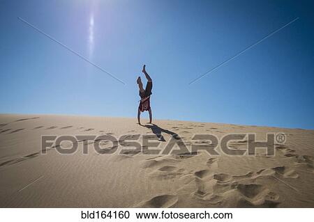 Stock Image - Caucasian teenage boy doing cartwheels on sand dune. Fotosearch